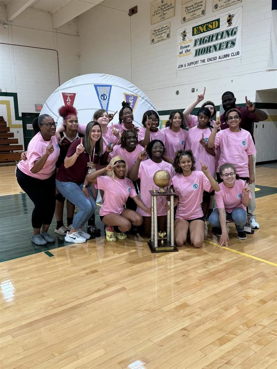  A group of students & coaches celebrate, posing with a large trophy & holding up #1 fingers.